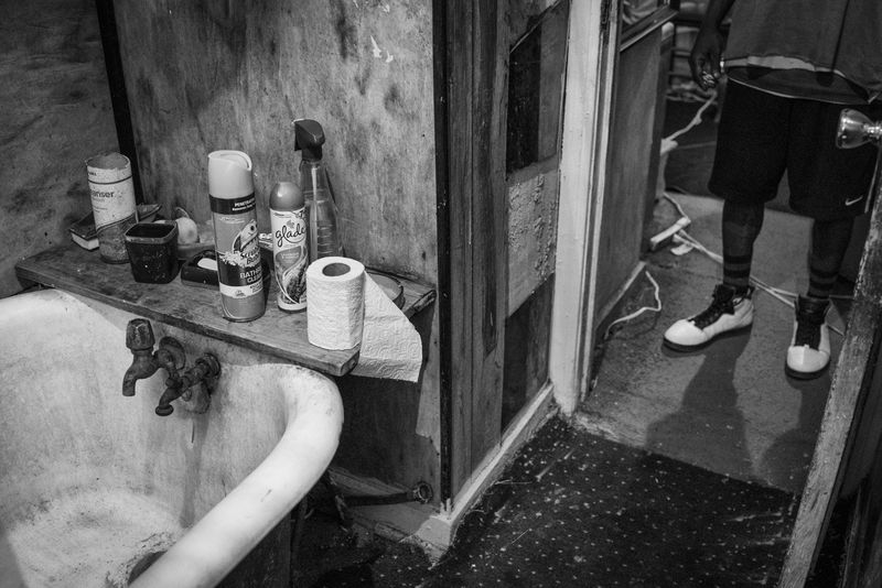 © Richard Sharum - “People” stands in front of his bathroom. Like other residents, he must use toxic groundwater to bathe with. 2018.