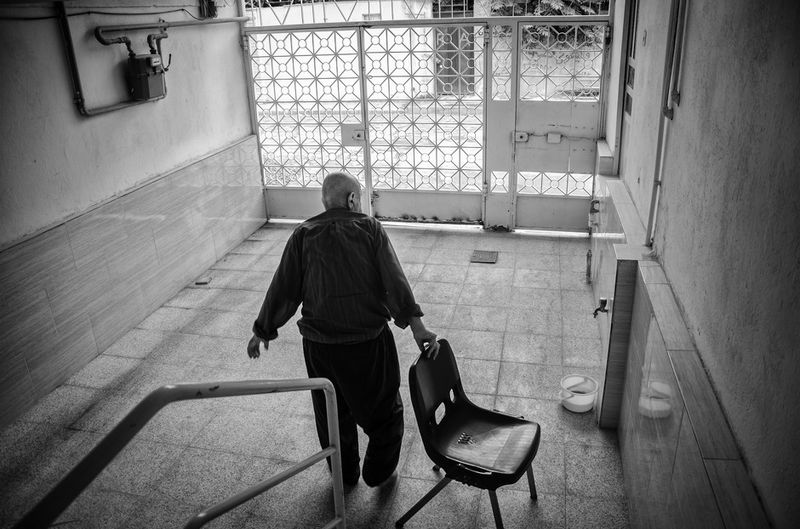 © Khashayar Sharifaee - Grandfather is dragging a chair outside of house so he can sit outside for some time and relax and breathe fresh air.