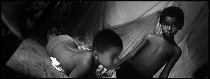 © Benjamin Rusnak - Children play on the single bed that an entire family must share in Santo Domingo, Dominican Republic.