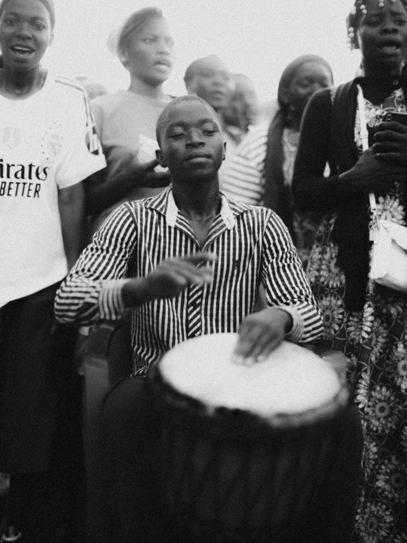 © Jeff Tidwell - A young man plays a djembe drum while others around him sing and dance