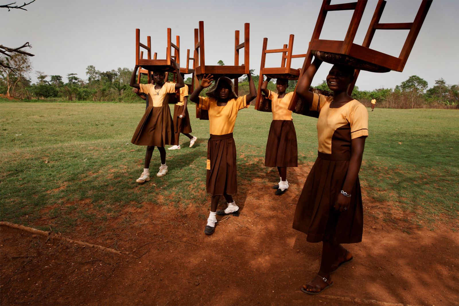 Schoolgirls in Ghana carrying chairs to the ceremony for the opening of the Maranatha Maternity Clinic