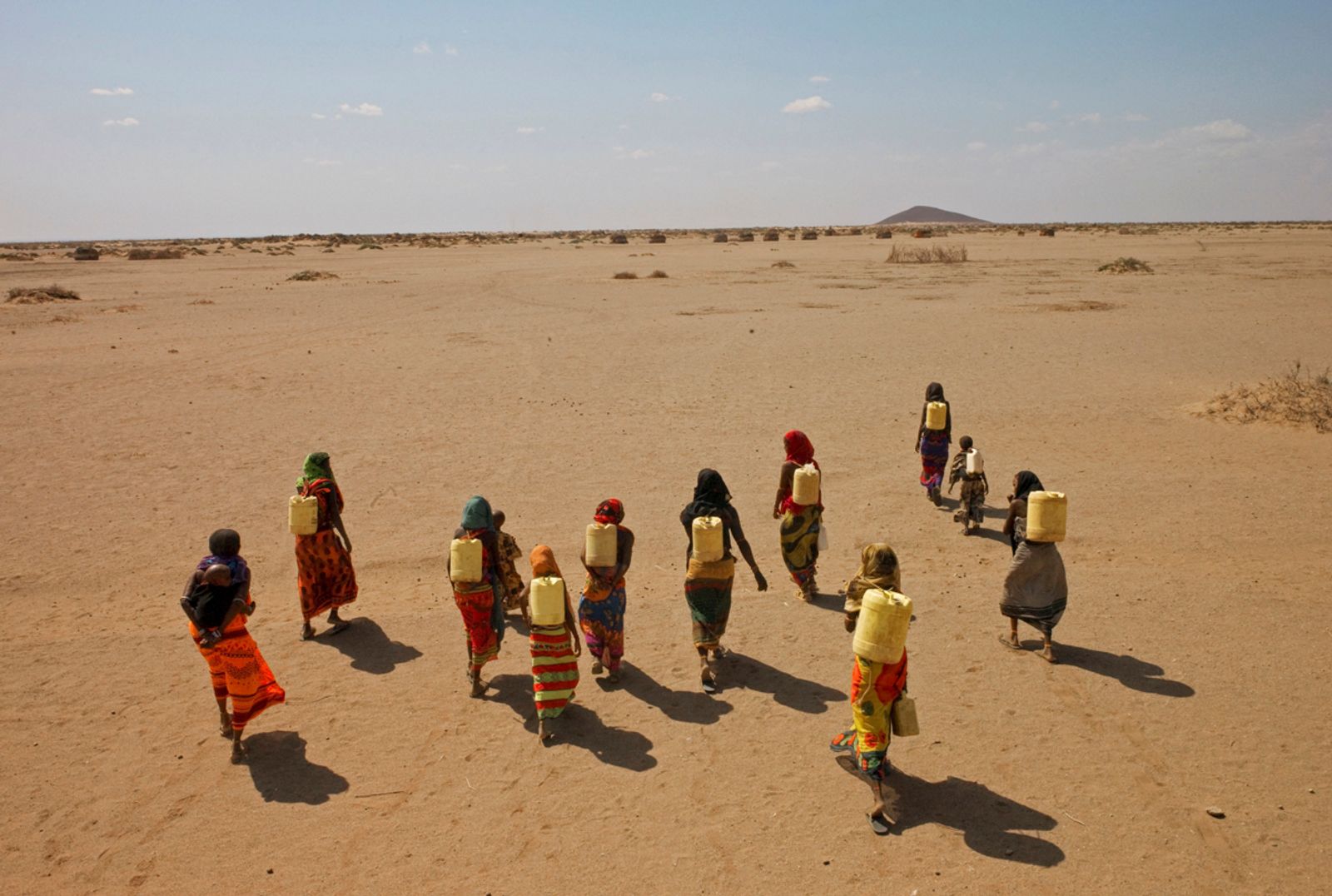 Gabra women carry jerry cans filled with murky water through desert plains in Kenya.