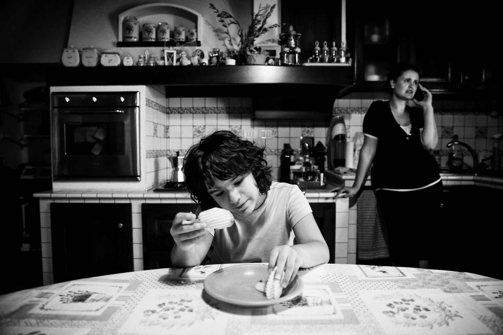 © BARBARA ZANON - Magione, Perugia, Italy - August 2016. Luisa has a snack at home in the kitchen, while being watched over by the babysitter
