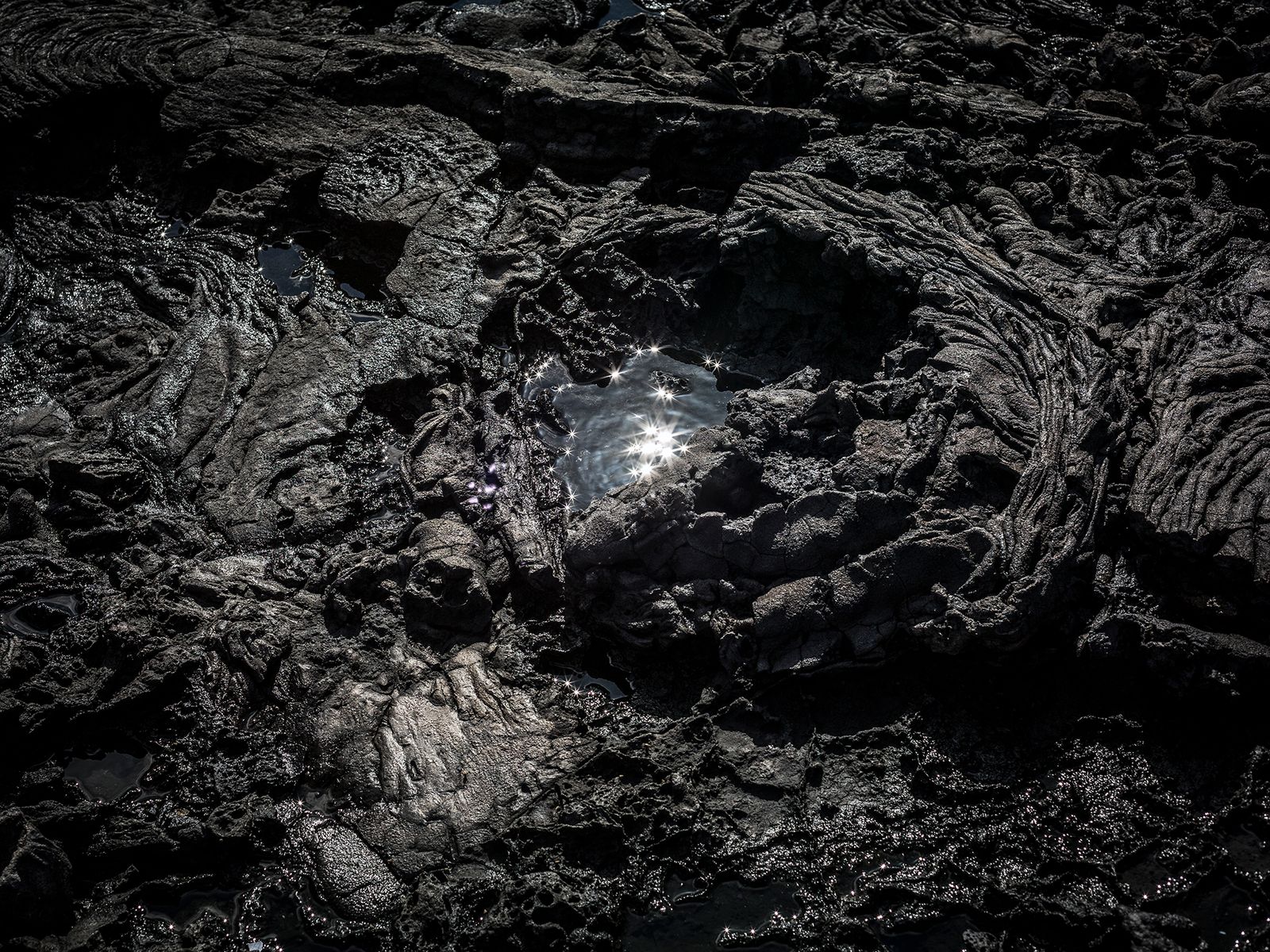 © Ilan Rabchinskey - Caldera. A pool of water reflects the sun in a pahoehoe lava formation in the Galapagos Islands.