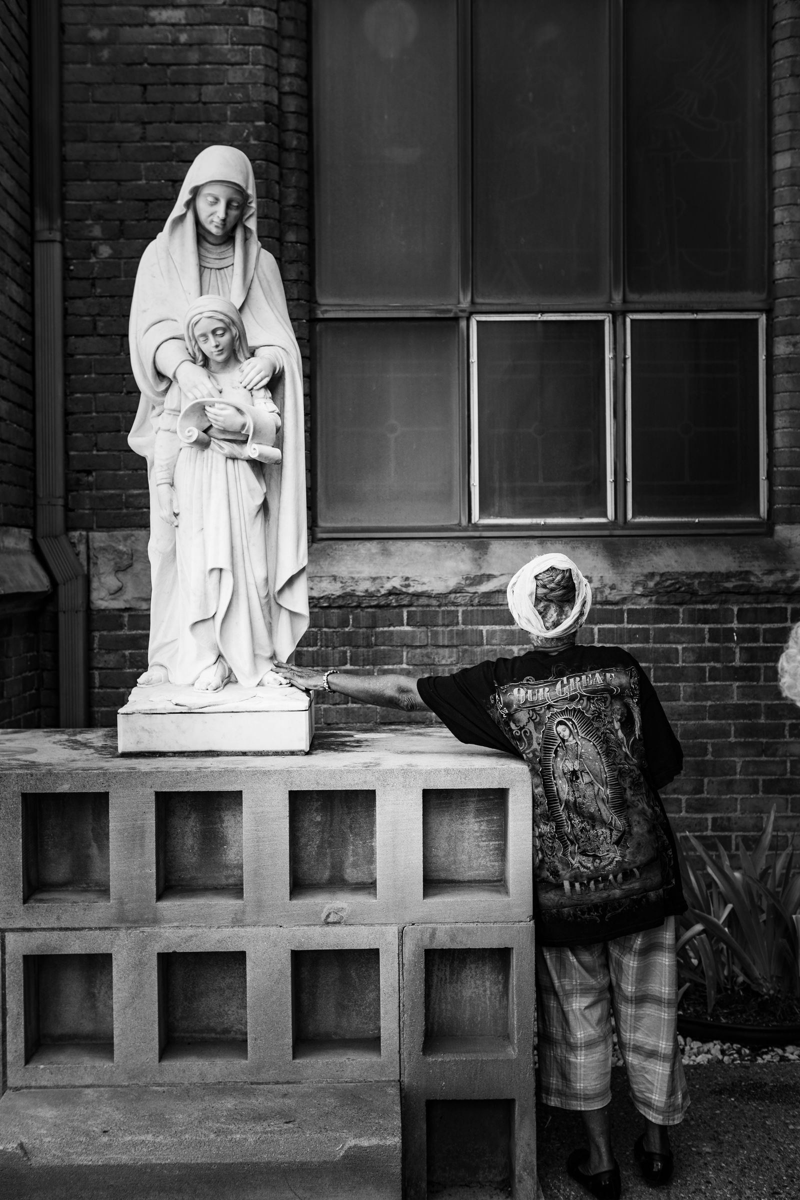 © JANICE MILHEM - Adi stands beside a statue outside St. Anne's Church touching a statue of Our Lady of Guadalupe.