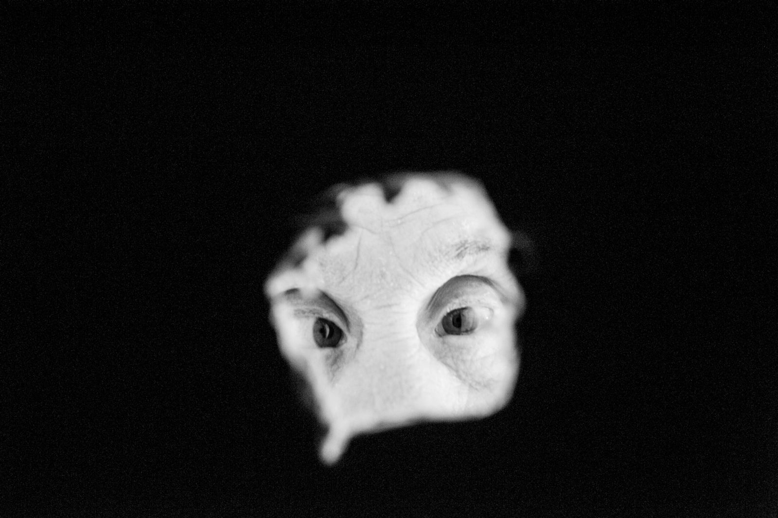 © Ilana Bar - The image is dark and in the center we see a hole where the eyes of someone with Down syndrome appear