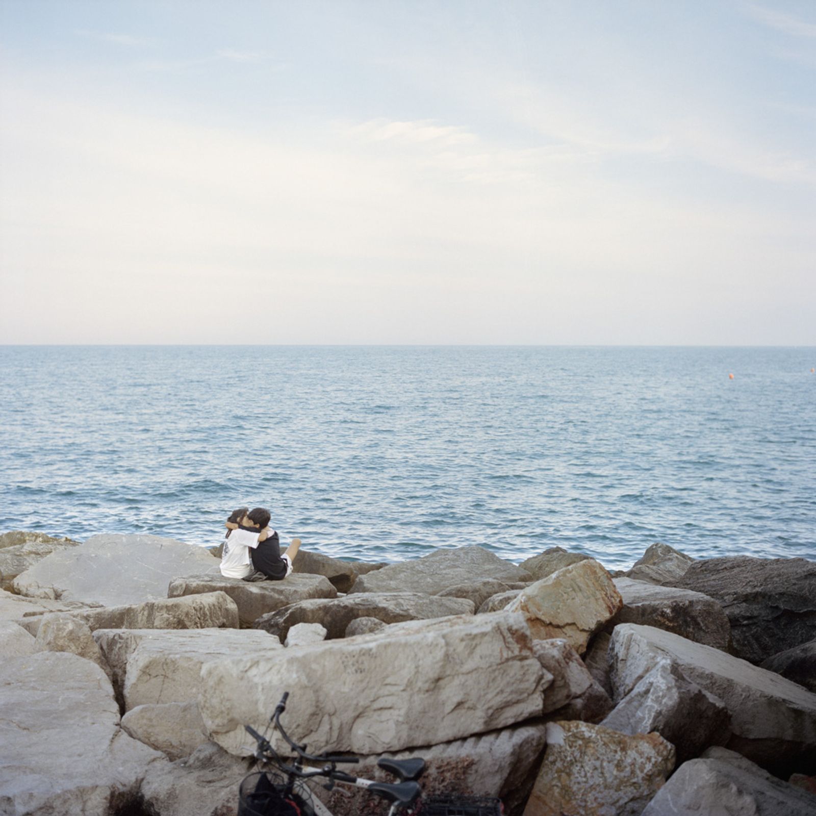 © Chiara Fossati - A very young couple of teenagers kisses in front of the sea at sunset.