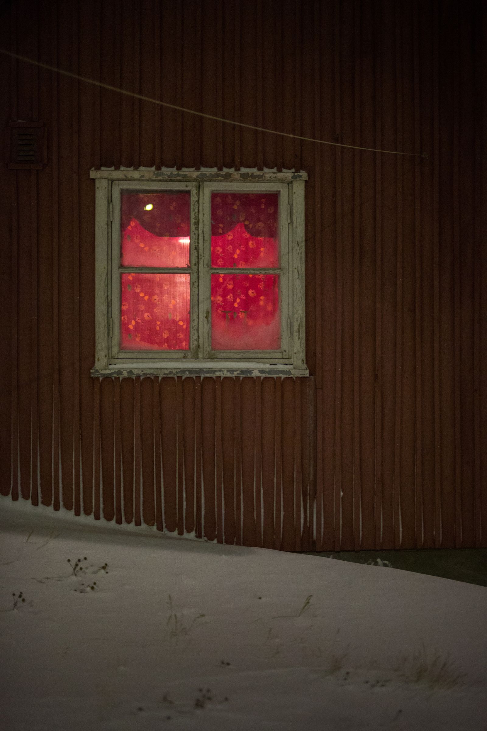© Lukas Kreibig - Red light shines through a window of one of the houses in Uummannaq on a cold winter night.