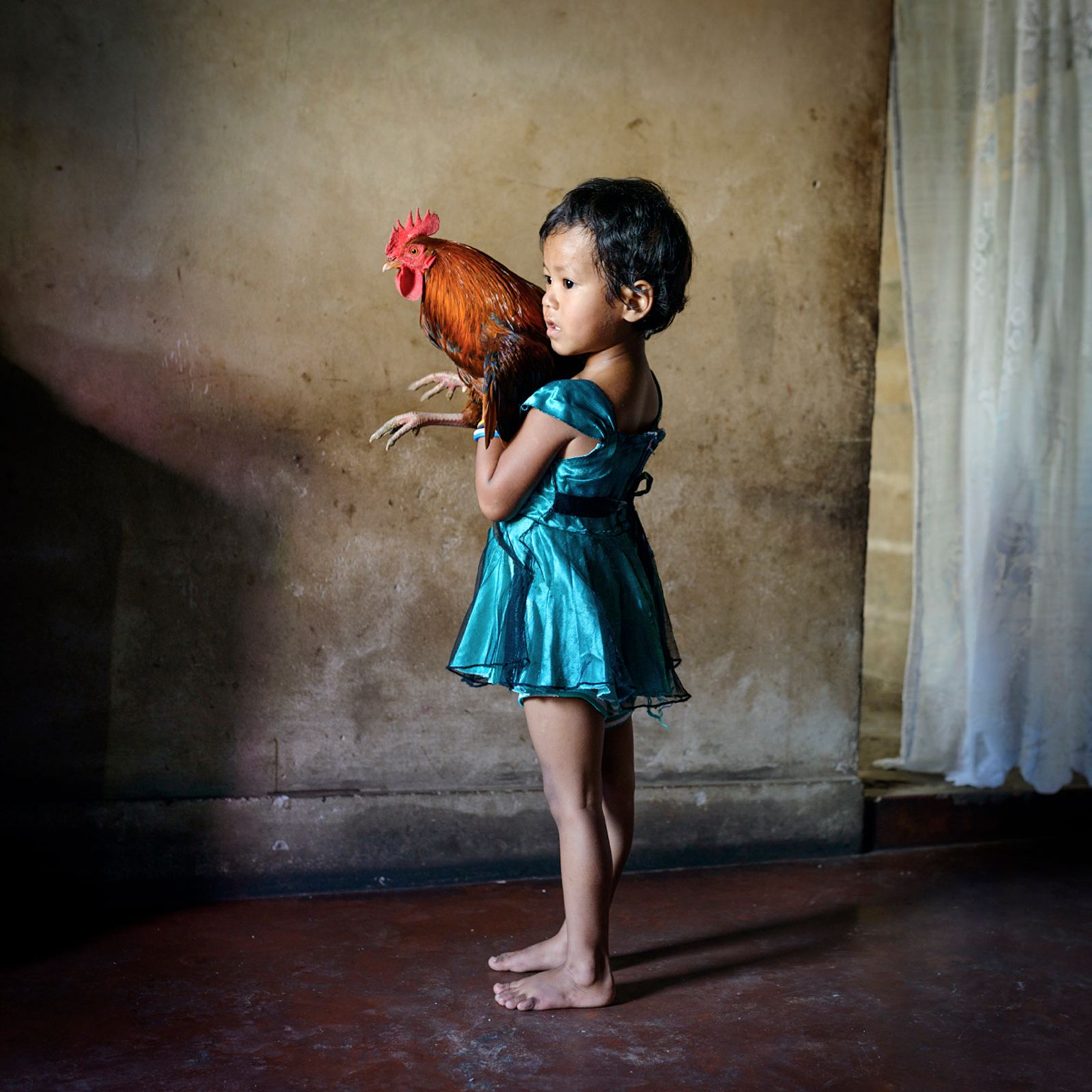 © Karolin Klüppel - Yasmin holds a rooster. She loves to catch and play with it after dawn.