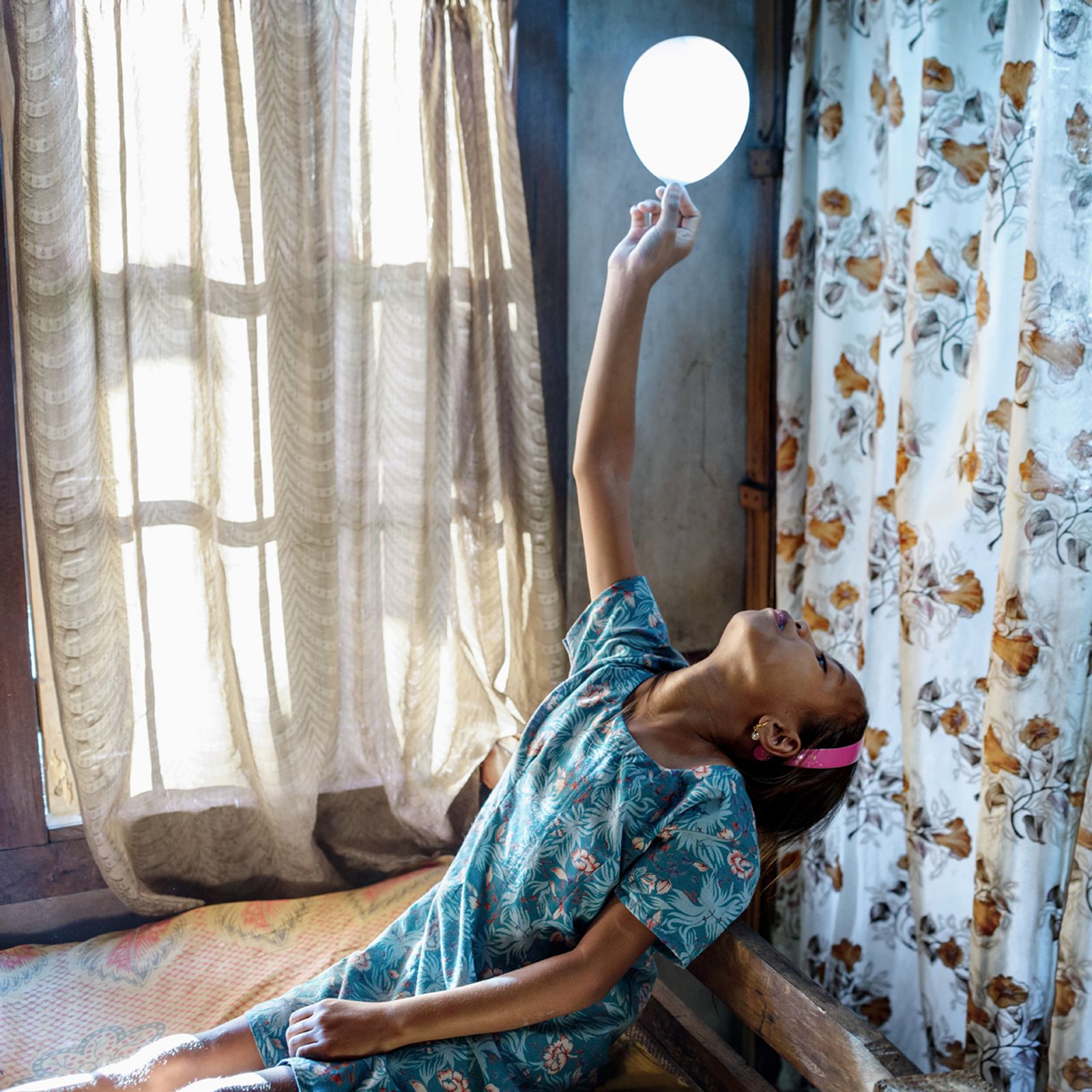 © Karolin Klüppel - Phida, 9 years old, is playing with a balloon in her bedroom. She is the oldest of three siblings.