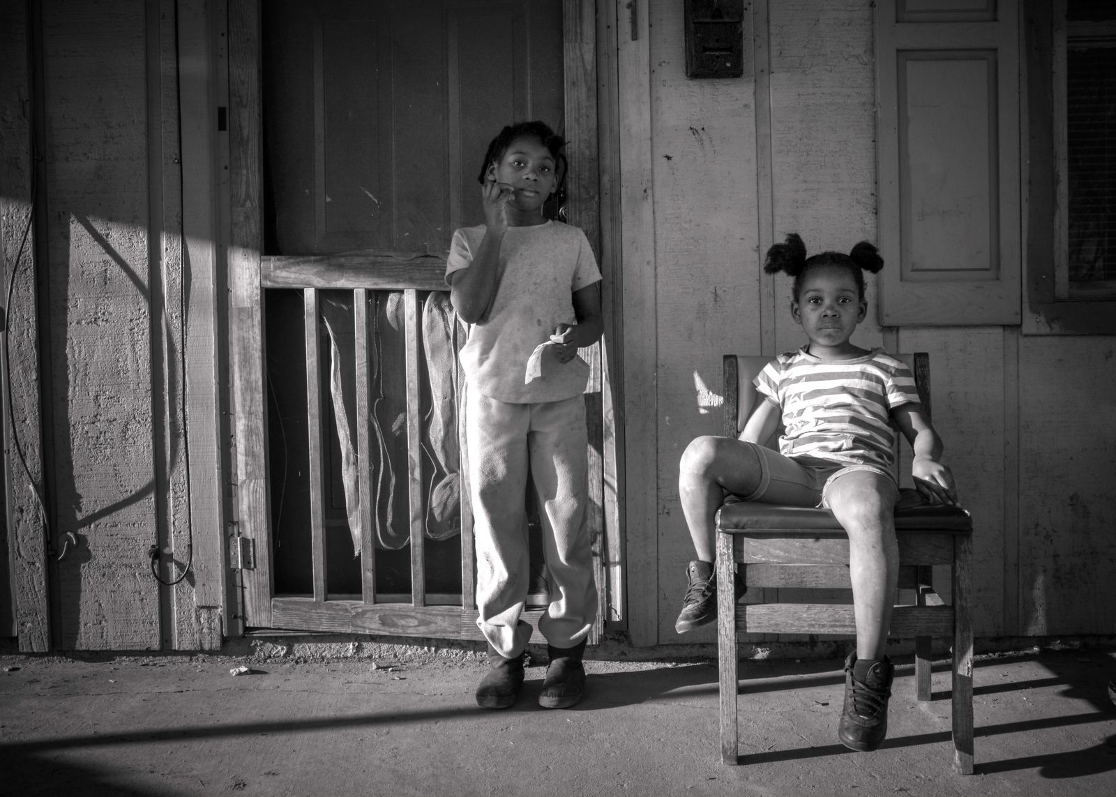 © Rebecca Moseman - Two Sisters. Two sisters play on the porch of their shotgun house in the community of Baptist Town.