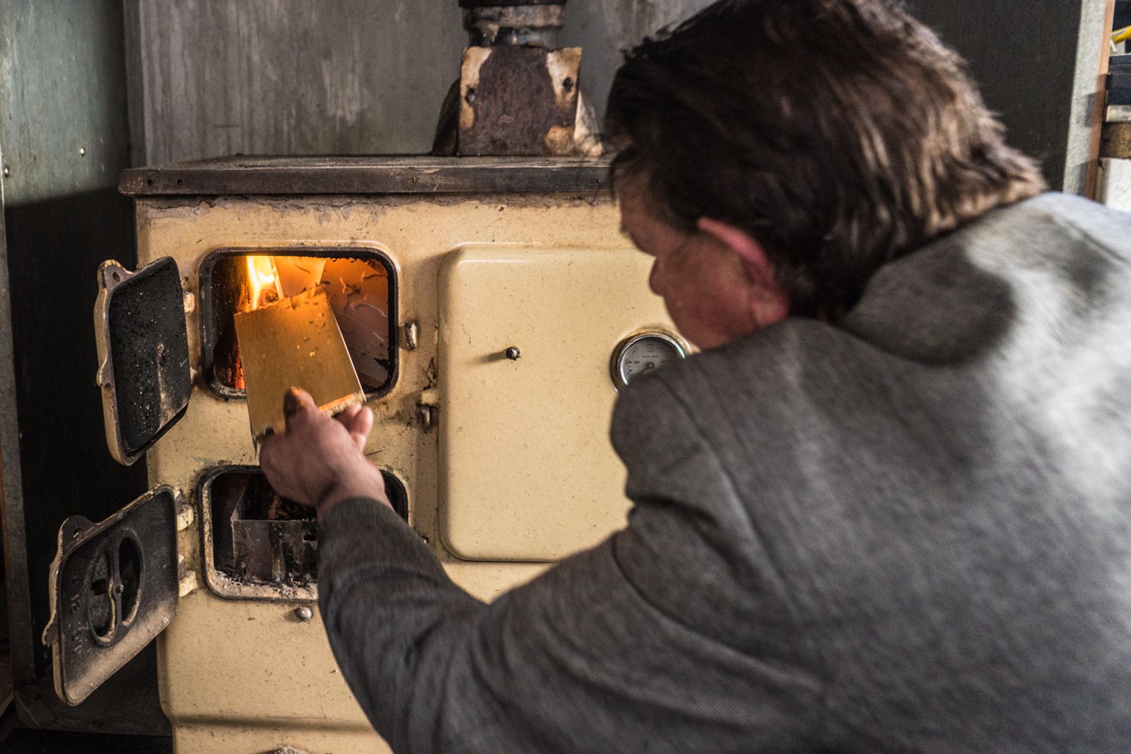 © Stephen Gerard Kelly - John (52) burns wood in a cast iron stove in his trailer for heat during the cold, wet Irish winter. 