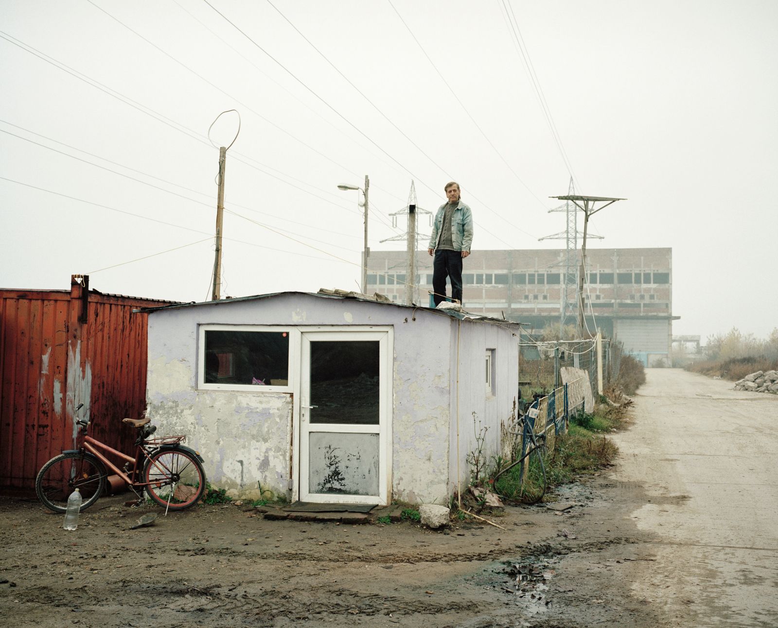 © Tommaso Rada - Romania, Giurgiu. A man working as security guard stand on a barrack in front of an abandoned factory that he watch