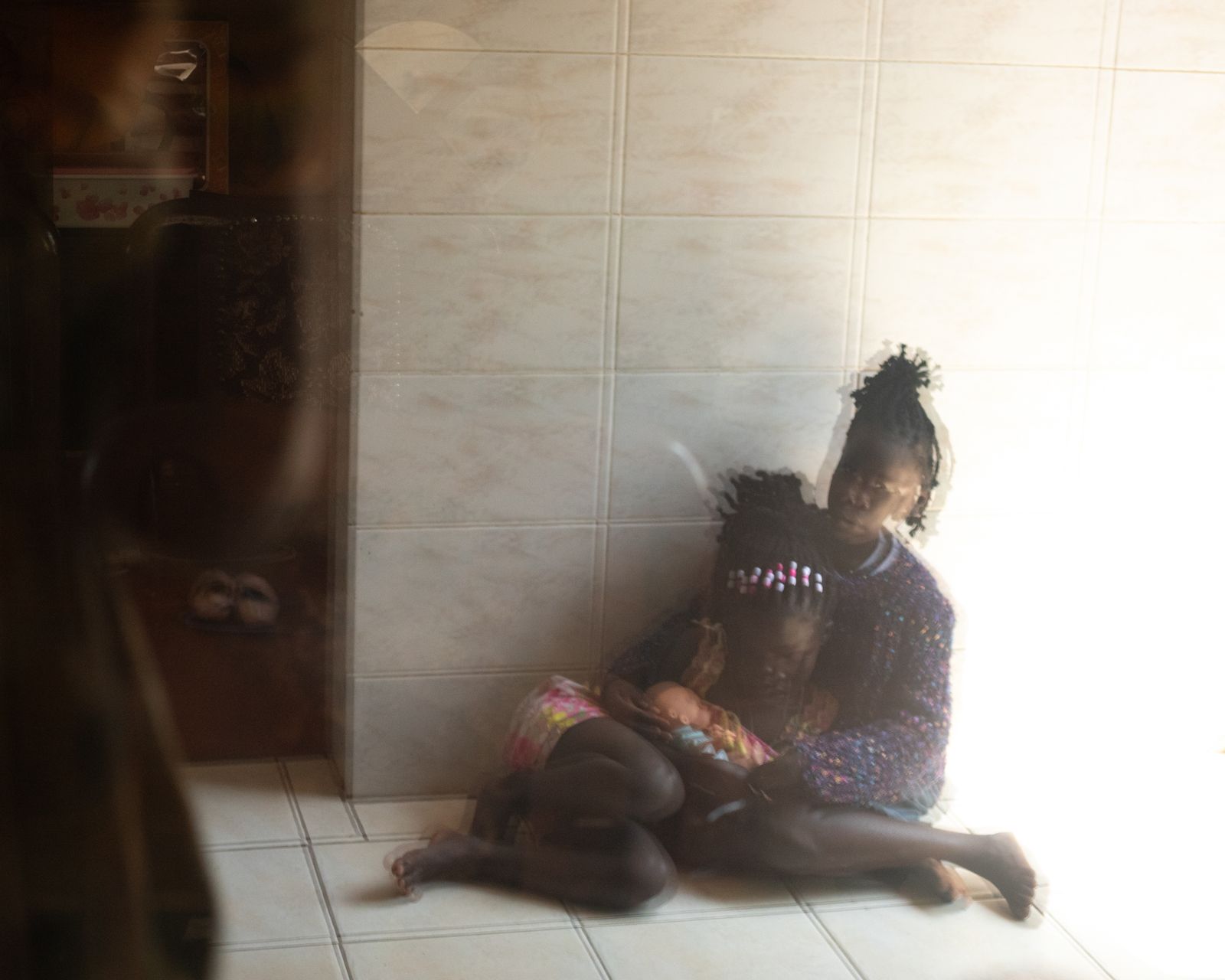 © DeLovie Kwagala - Blessing* 8 comforts the youngest survivor, Immy* 7 at the lily of the valley shelter.