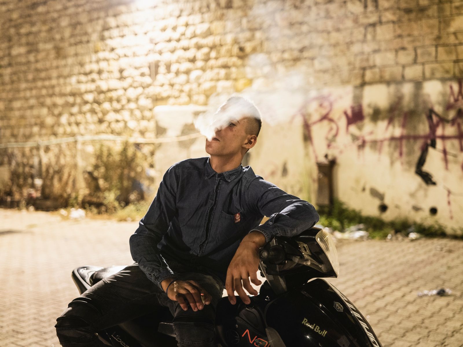 © Sebastian Wells - Danilo smokes on his motorbike. „He´s famous at the police office“, a few friends of him tell me. Augusta, August 2019.