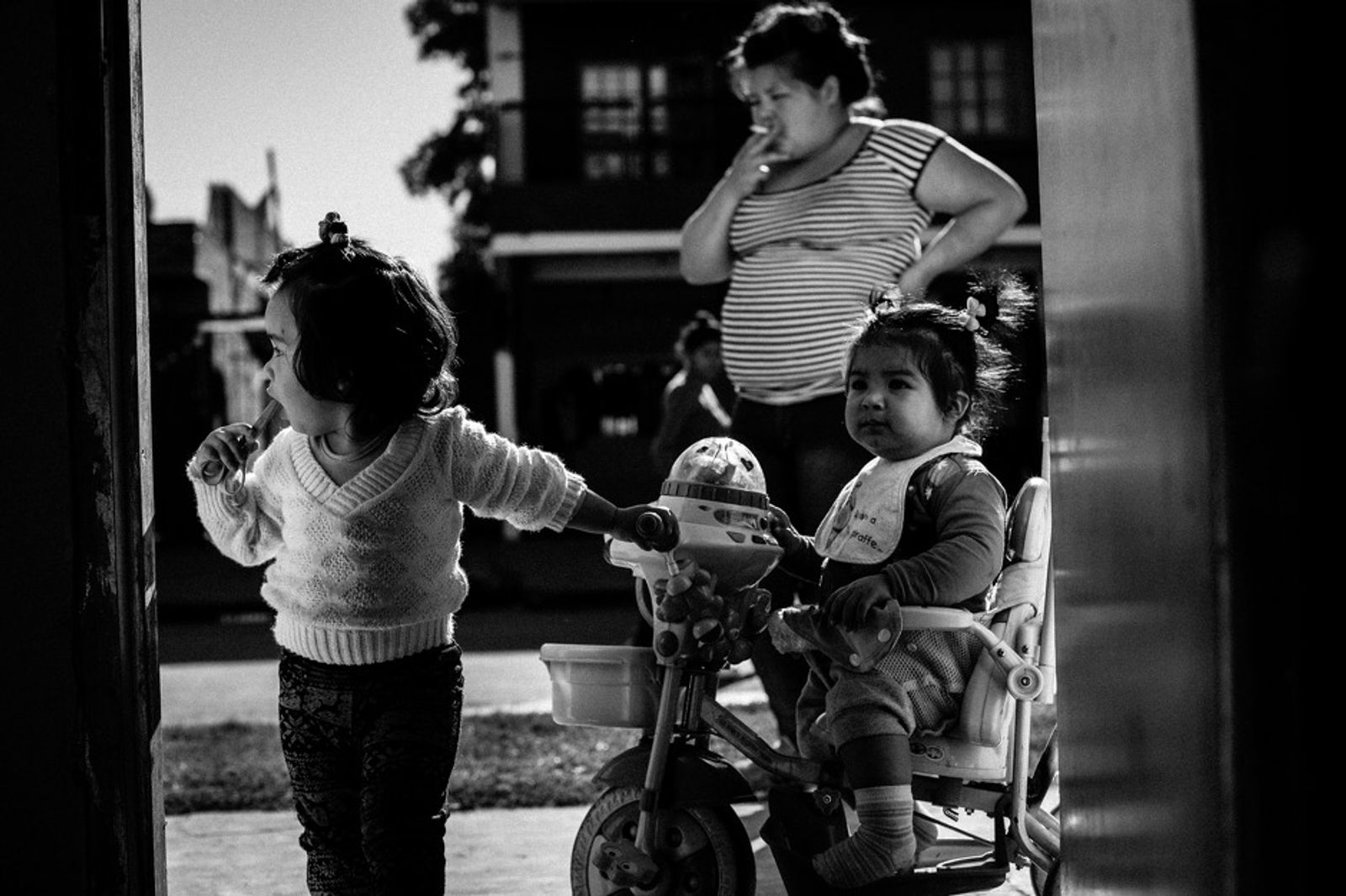 © Sarah Pabst - Stefi smokes a cigarette on the street in Monte Chingolo, while Maite and Mia play together.