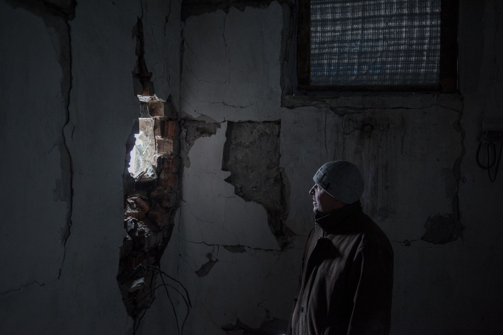 © Valery Melnikov - . A local resident looks at a hole from a shell in the wall in the village of Donetskyi, Lugansk region