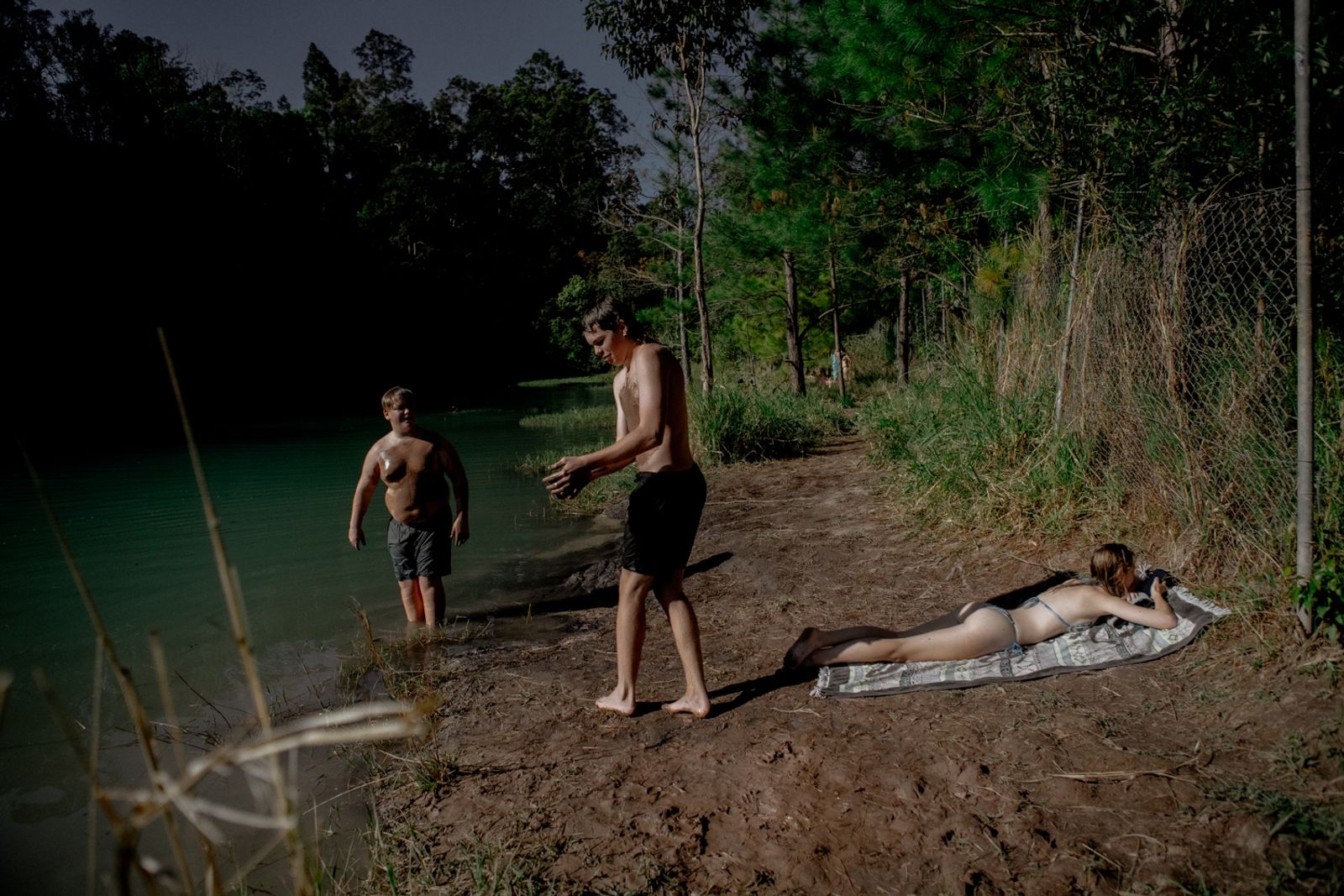 © Tajette O'halloran - Boys cover their bodies in mud while a girl sunbathes and looks at her phone
