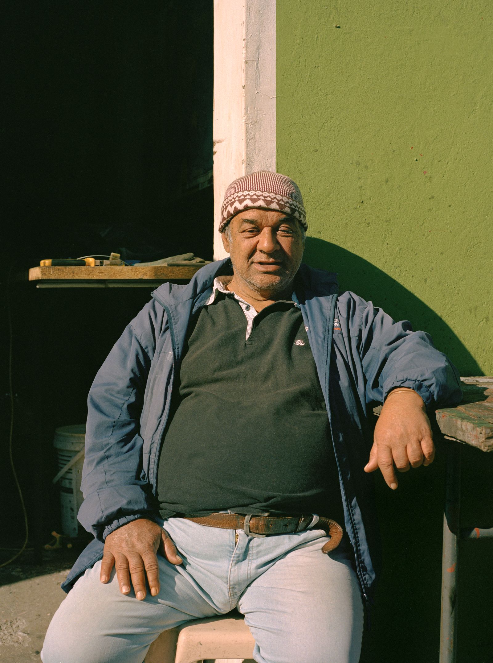 © Ayesha Kazim - An older member of the community soaks up some sun while sitting outside of his garage on Van Der Meulen Street.