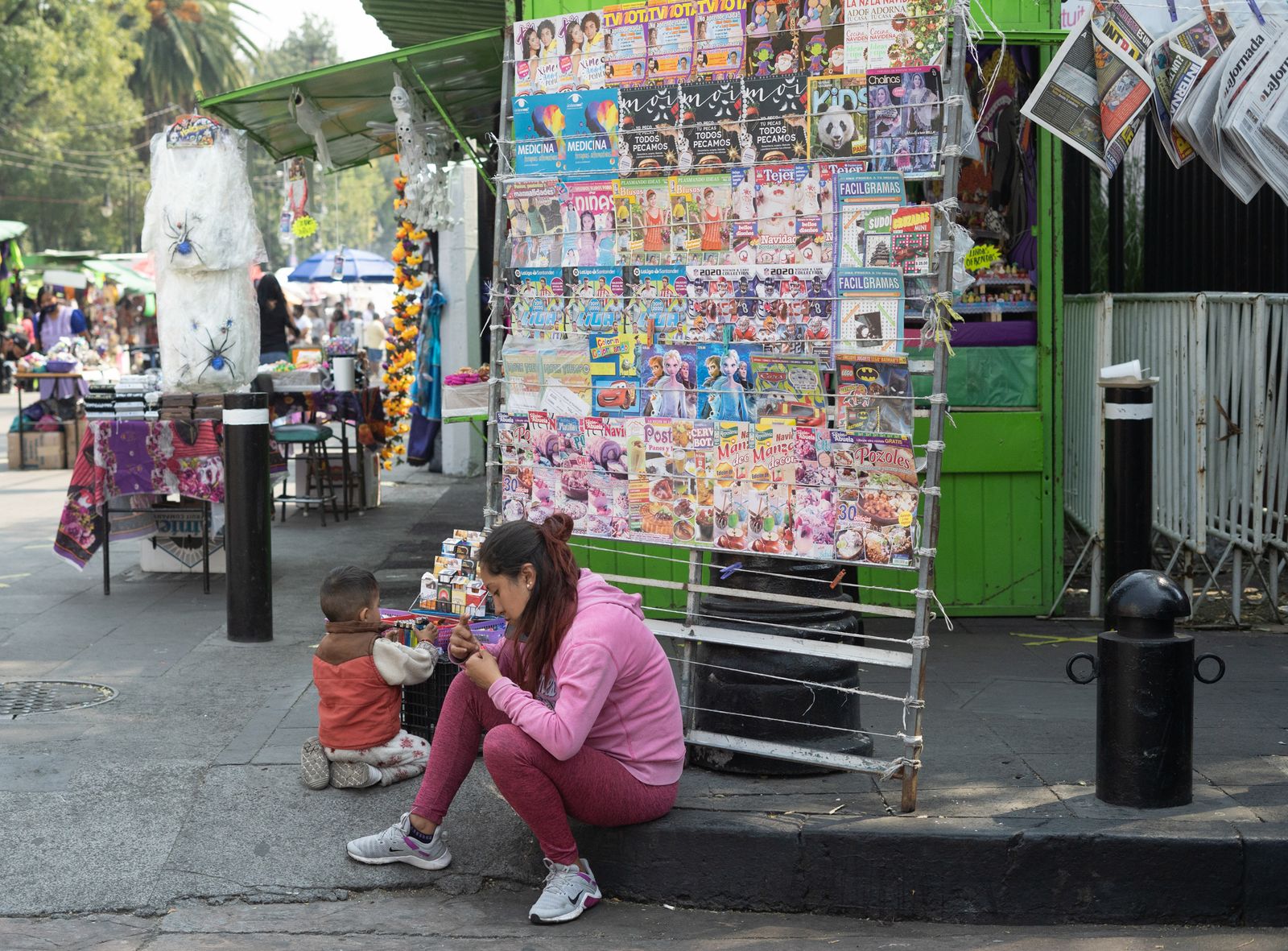 © Roxanne Munson - A woman sitting on a curb selling magazines with a little boy next to her playing.