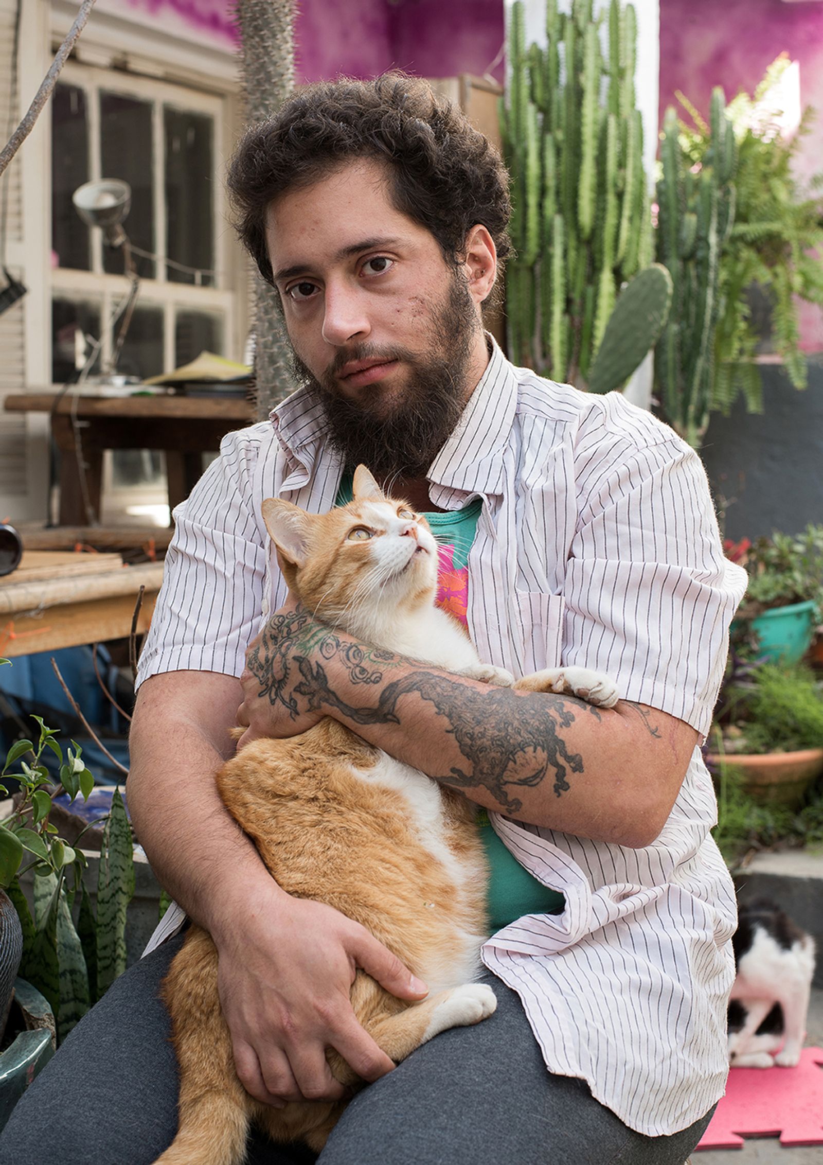 © Camila Falcão - Juno, writer and animal lover, sits at his yard with Deleuze, one of his cats, on his lap