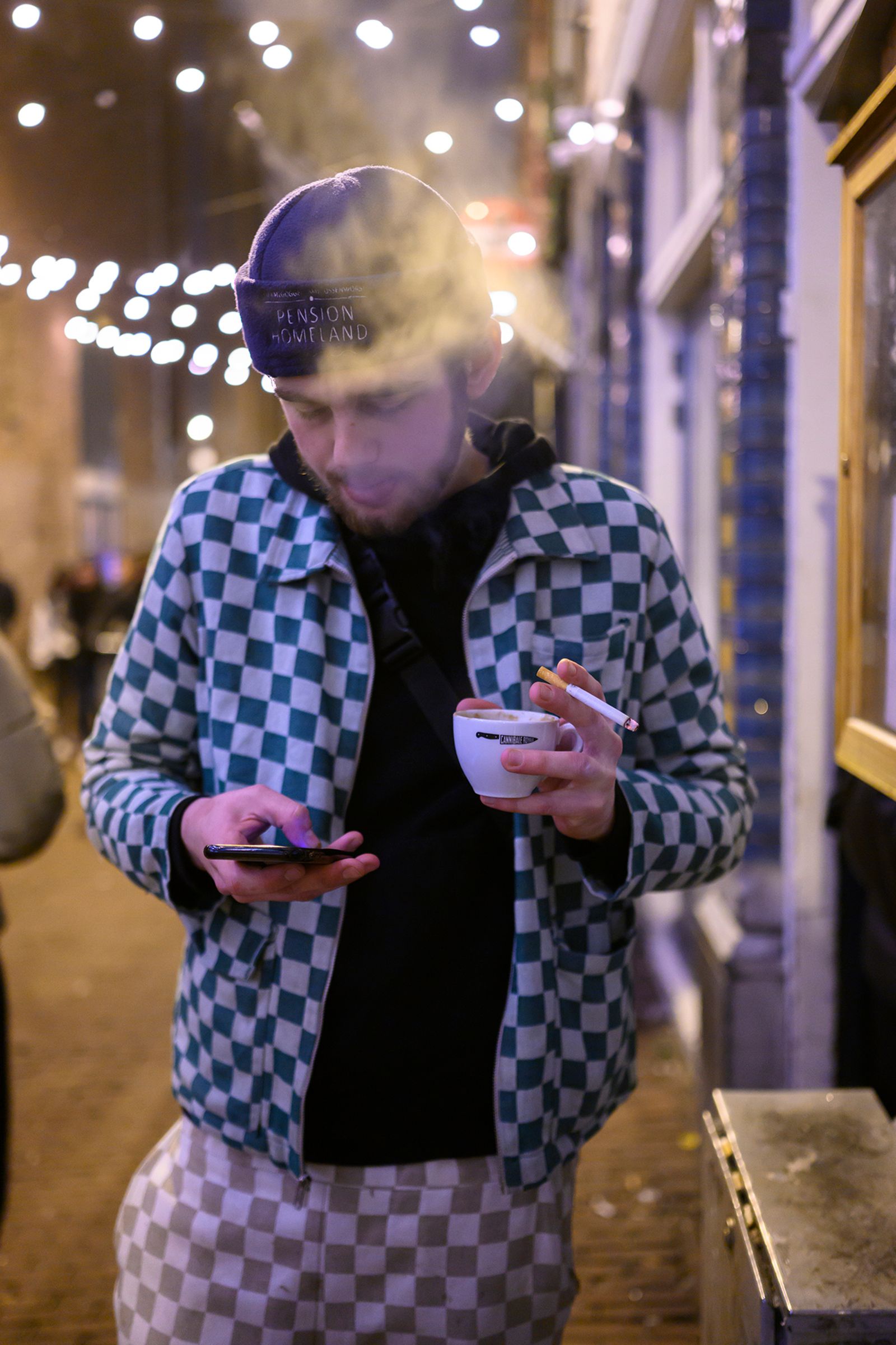 © Els Zweerink - Sammie at night in front of a club with a coffee, a cigarette and his mobile.