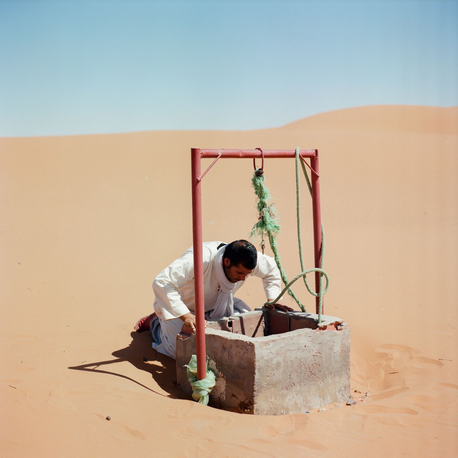 © M'hammed Kilito - A man looking for water in a well surrounded by sand dunes at the oasis of Merzouga