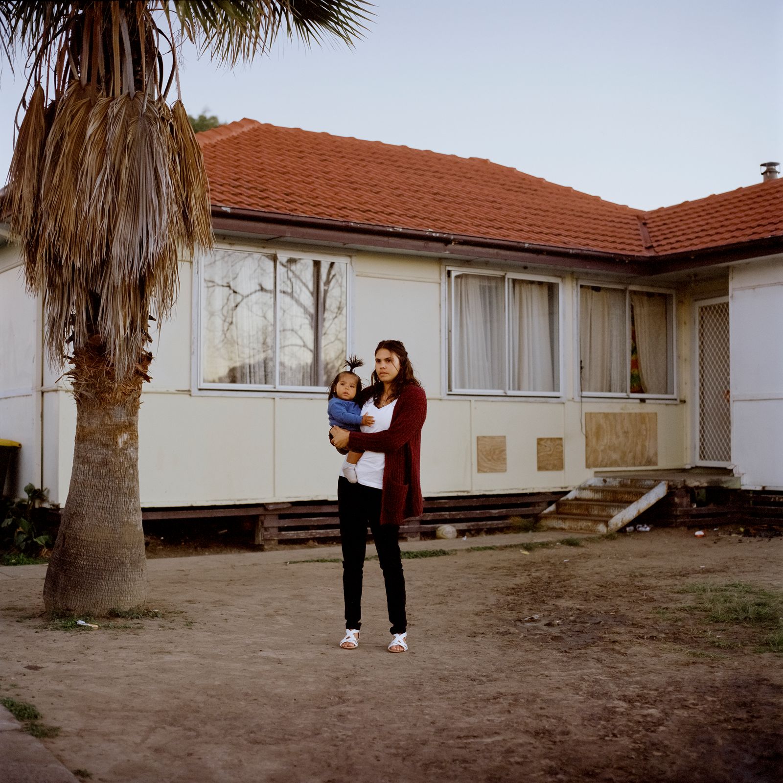 © Raphaela Rosella - Rowrow's sister Kayla holds her son Kaylan in the front yard of their parent’s home in Moree, New South Wales, Australia.