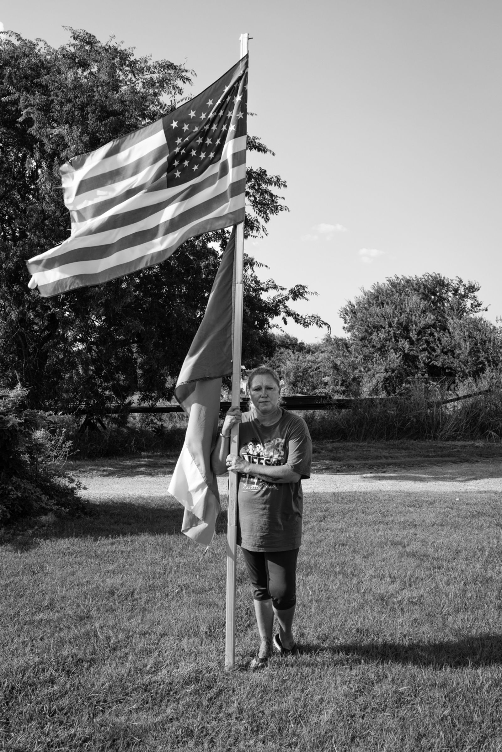 © Richard Sharum - A woman stands next to the flag pole in her front yard. Wichita Falls, Texas. 07.28.2021