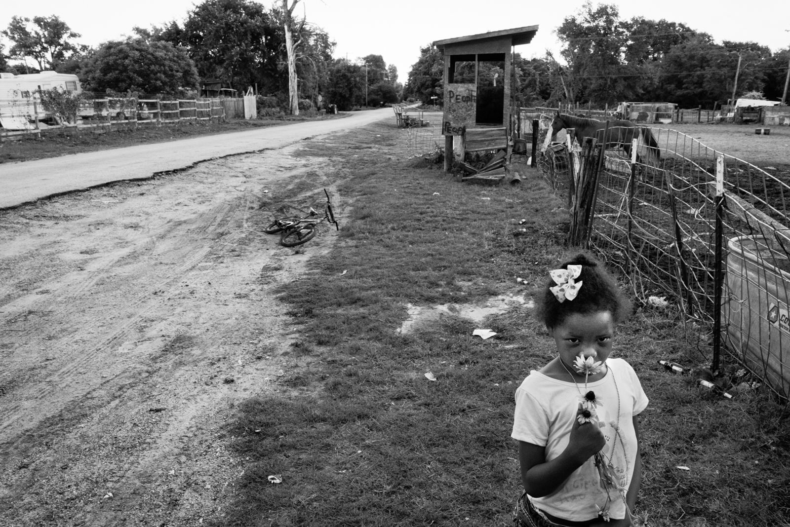 © Richard Sharum - A young girl smells a flower on Bunche Street. She is one of six children that live in Sand Branch. 2019.