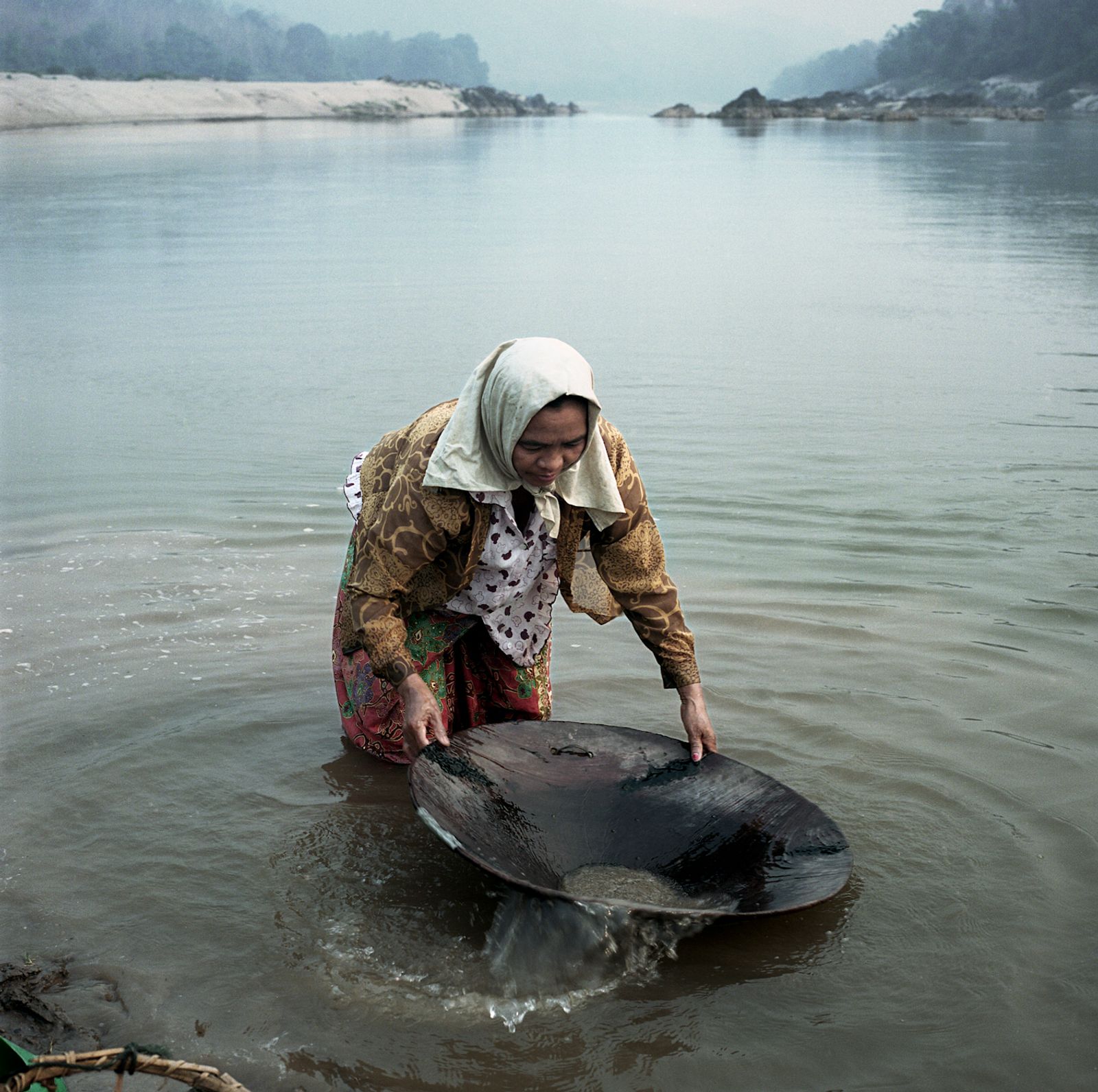 © Huiying Ore - Villager Ngoi, 63 years old, pans for gold along the Mekong riverbank.