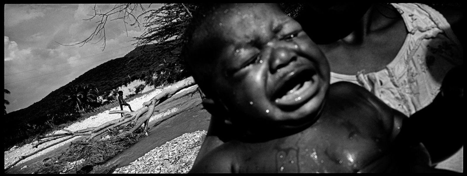 © Benjamin Rusnak - A baby cries after his daily bath in a river along the border of Haiti and the Dominican Republic.