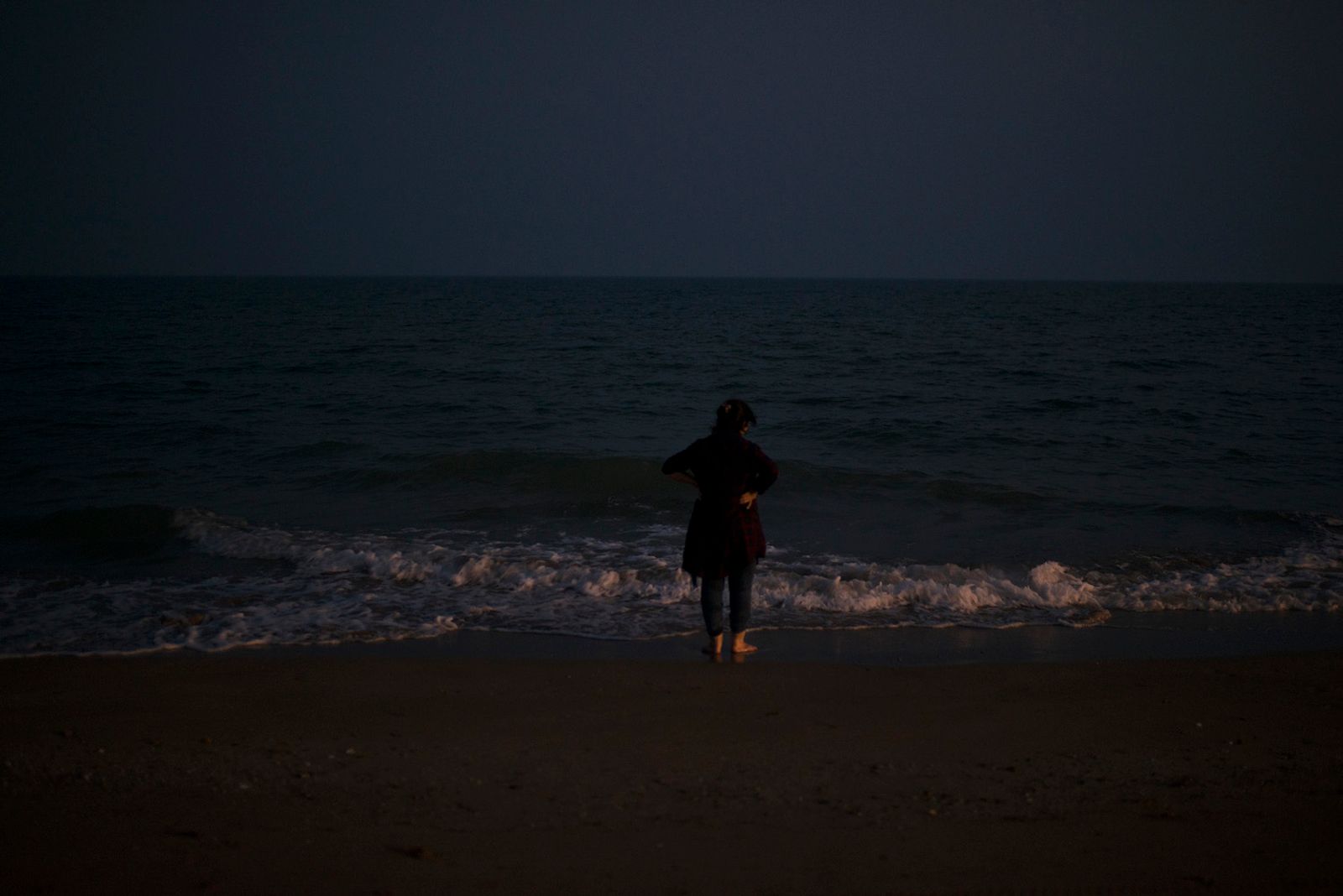 © Marjan Yazdi - A woman standing in front of a very quite beach of the Persian gulf, while uncovering her hijab.