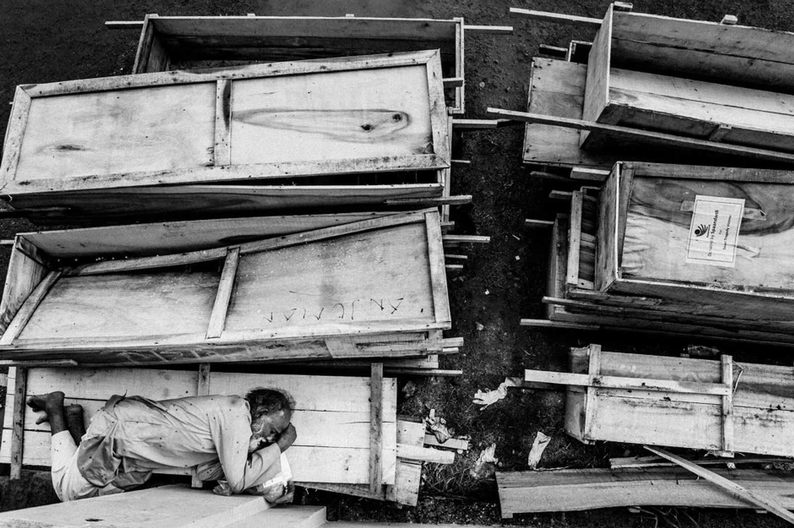© Rahul Talukder - An old man sleeps on coffins at a makeshift morgue in a schoolyard near Rana Plaza.