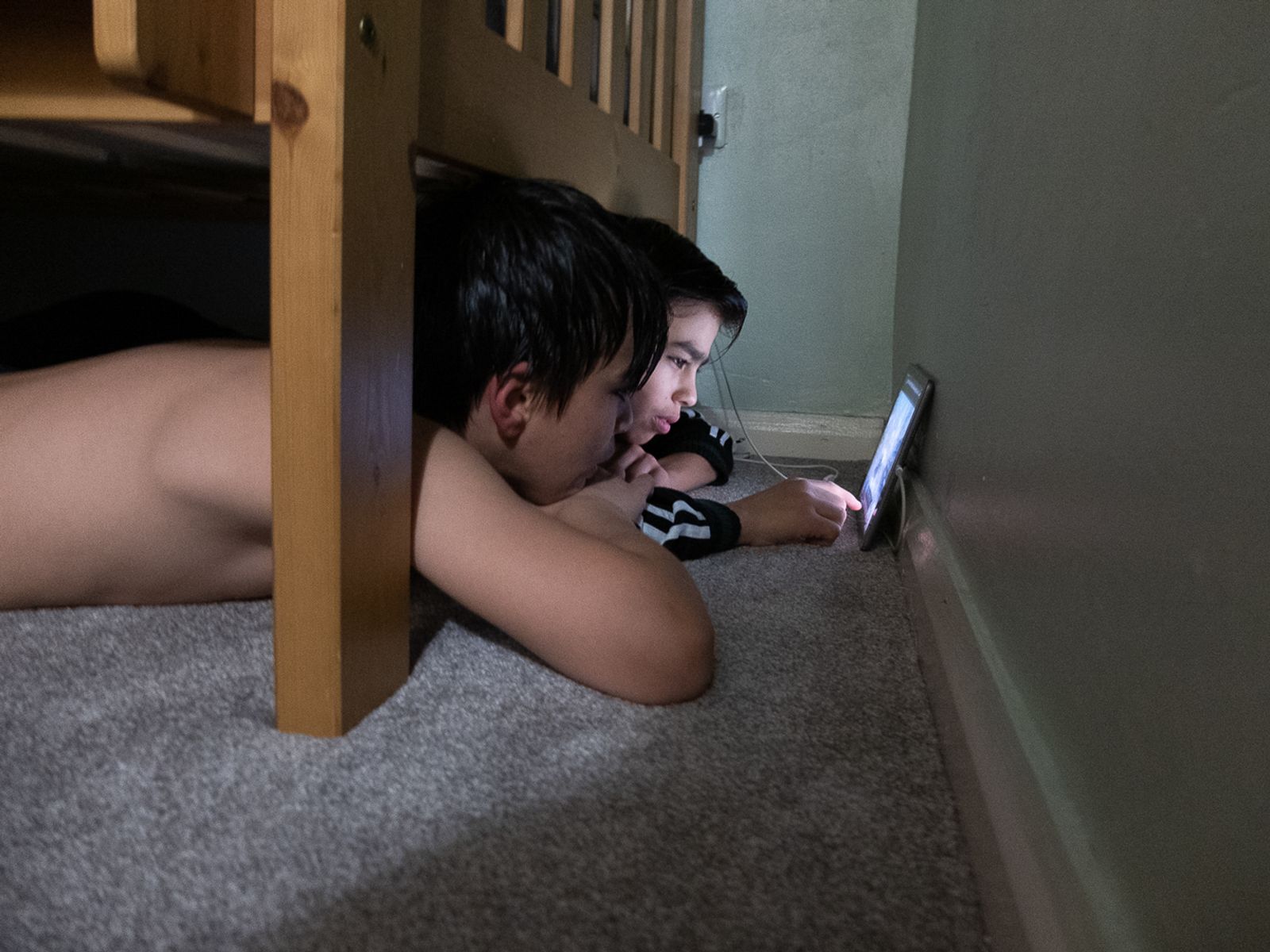 © Rich Wiles - Photo - Ruba al-Hindawi. Mustapha (right) and Yazan watching a tablet under their bed during UK lockdown restrictions.