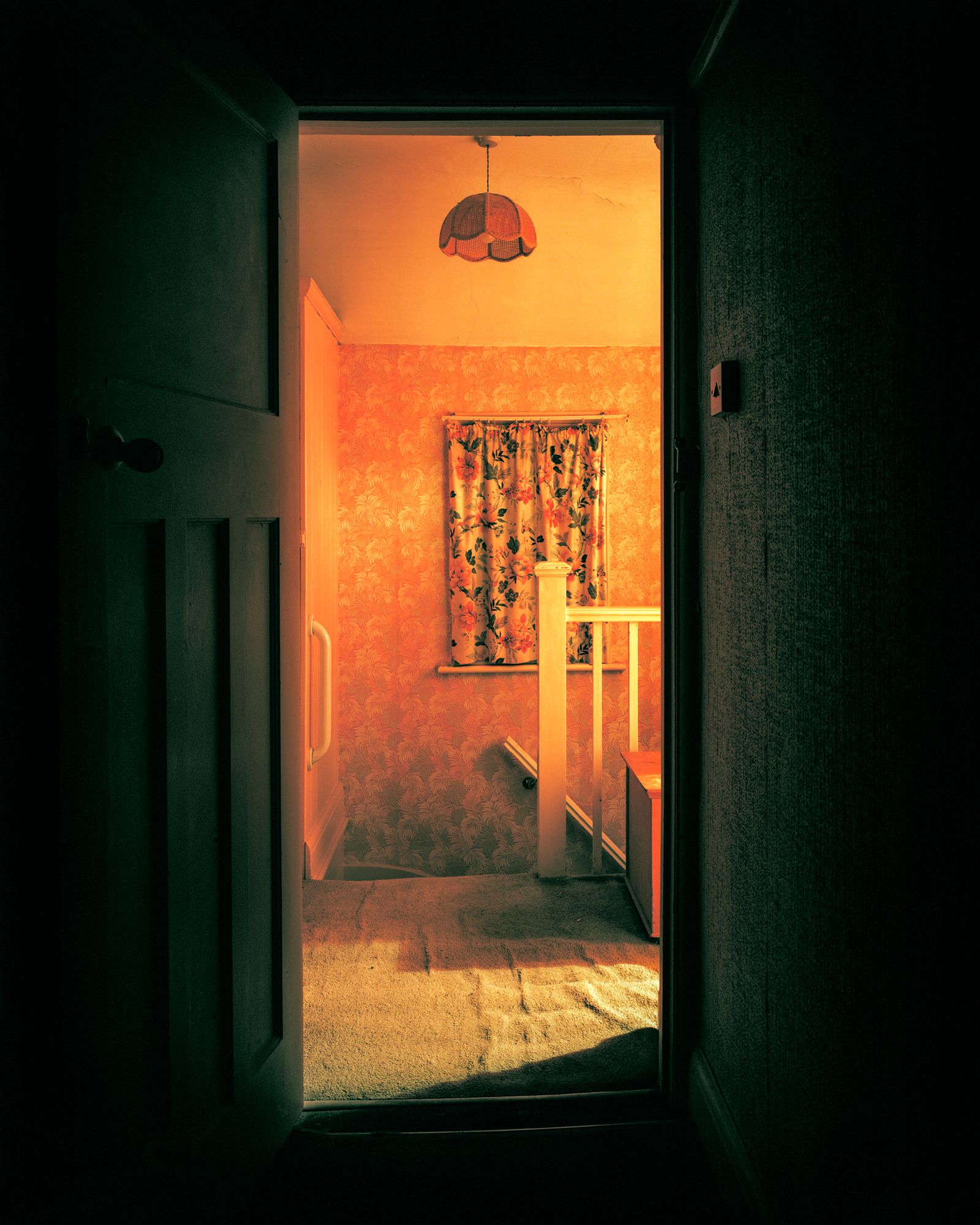 © Oliver Woods - A view of my childhood bedroom door opened and looking out onto the landing with some of the lights on.