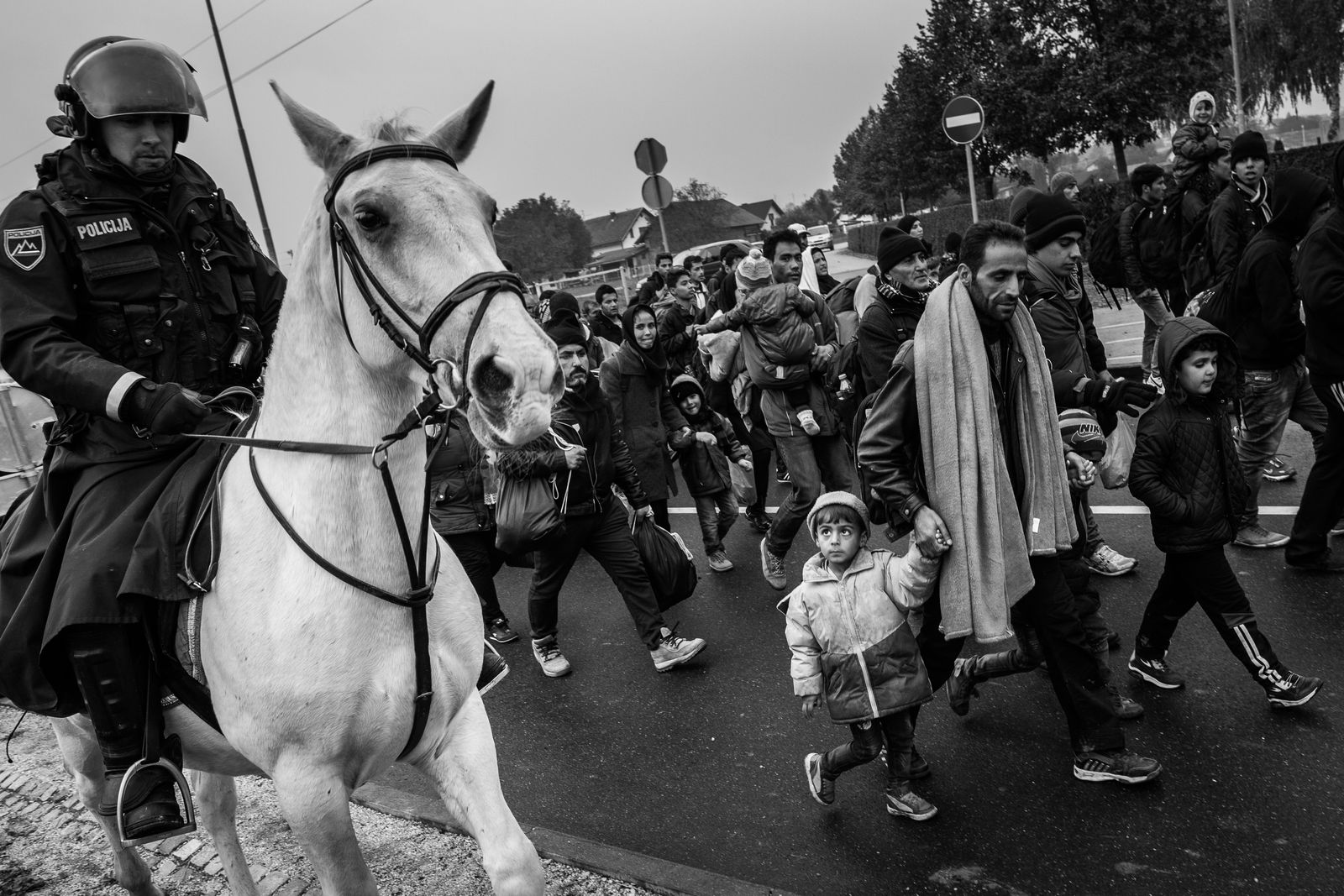 © Kemal Jufri - Refugees, among them children walk through the village of Dobova, Slovenia escorted by a horse-riding Slovenian police.