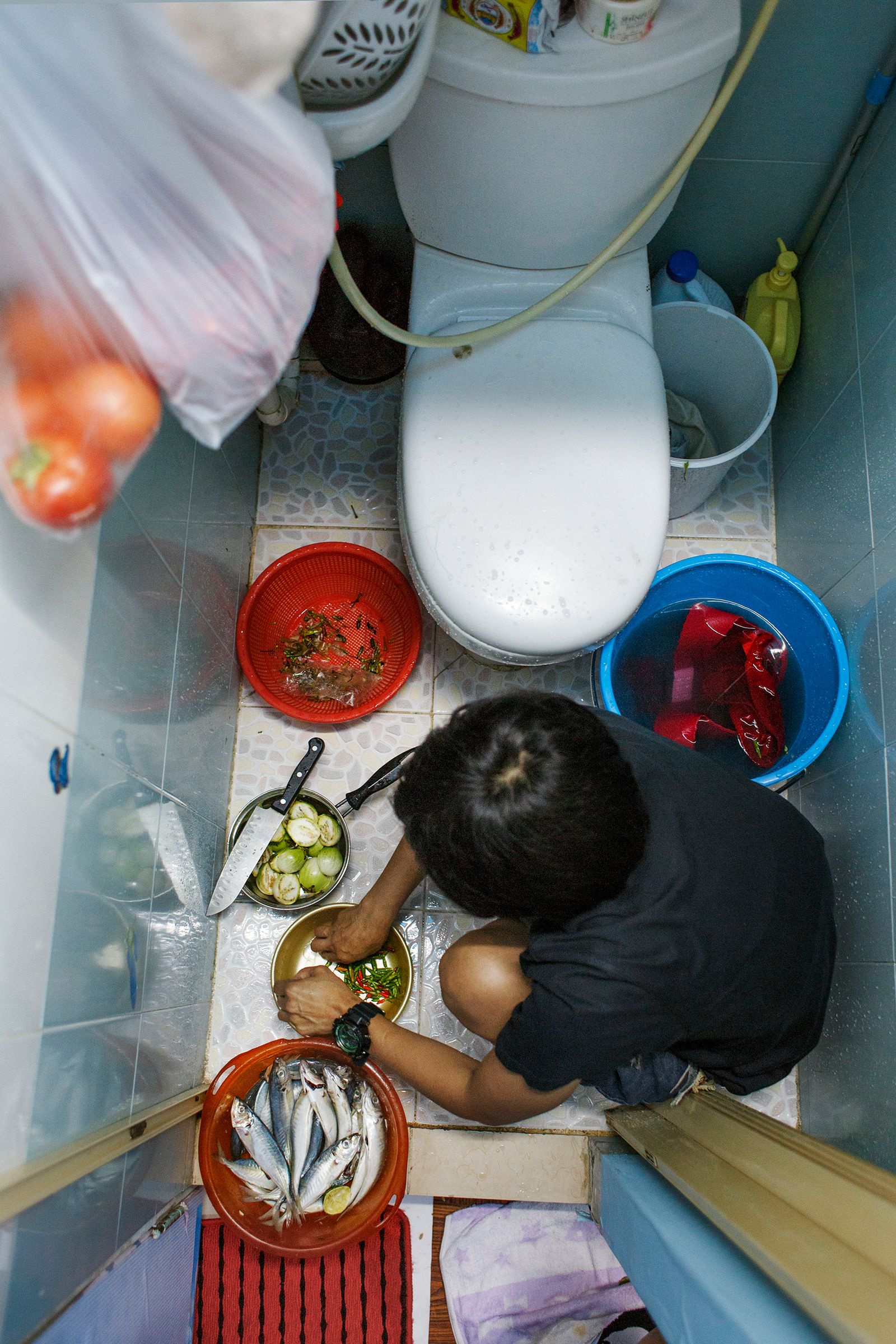 © Rebecca Sampson - Preparing dinner in the toilet/kitchen - 5sqm apartment shared by 2 housemaids in Hong Kong