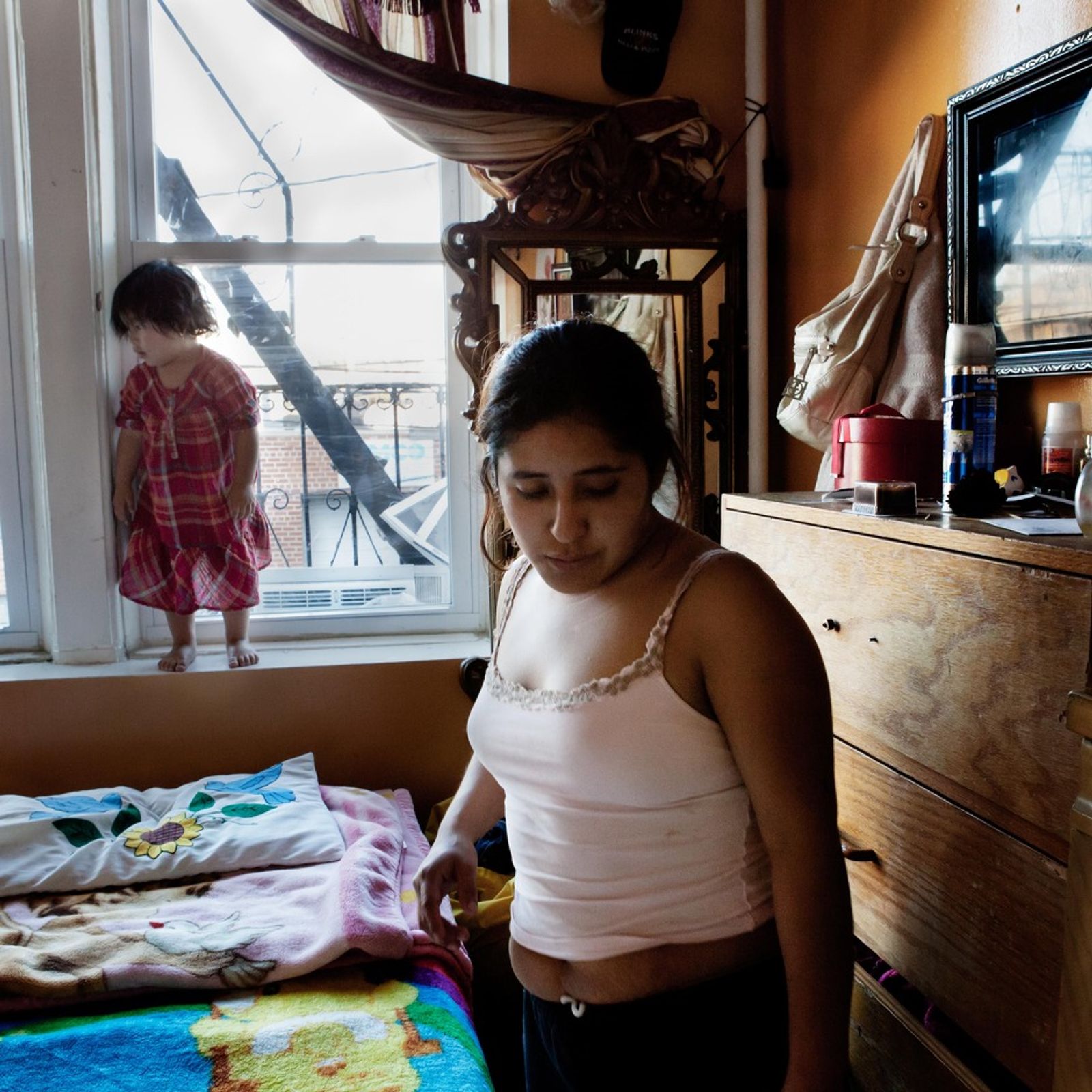 © Ruth Prieto - Juanita on her daily activities while her daugther Lluvia plays around the window and the bed.